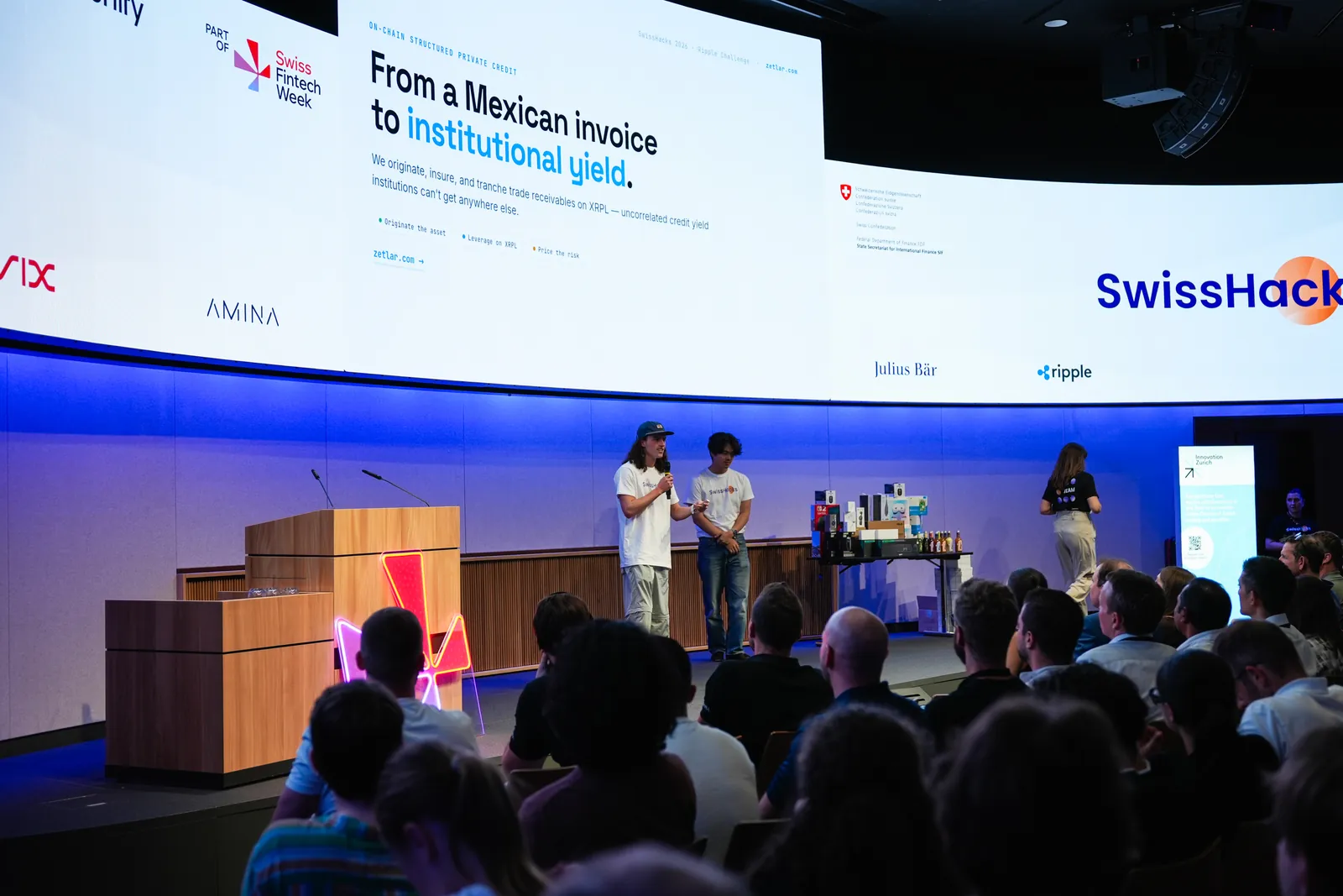 Zetlar being pitched on the SwissHacks main stage, screen reading 'From a Mexican invoice to institutional yield'
